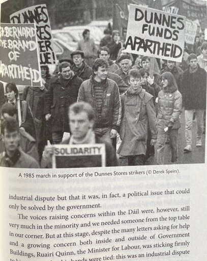 Protester hold signs saying "Dunnes Funds Apartheid" and similar messages.