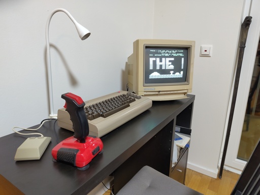 a clean desk with several C64 peripherals e.g. a mouse, quickshot 2, the commodore 64 itself and a commodore 1084S colour monitor.