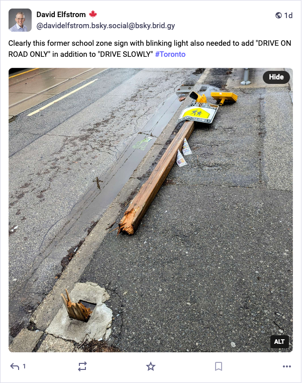 Fallen sign on a sidewalk next to a road showing the broken post. It had a blinking yellow light on top, a bright yellow triangle with walking schoolchildren silhouette and the words DRIVE SLOWLY