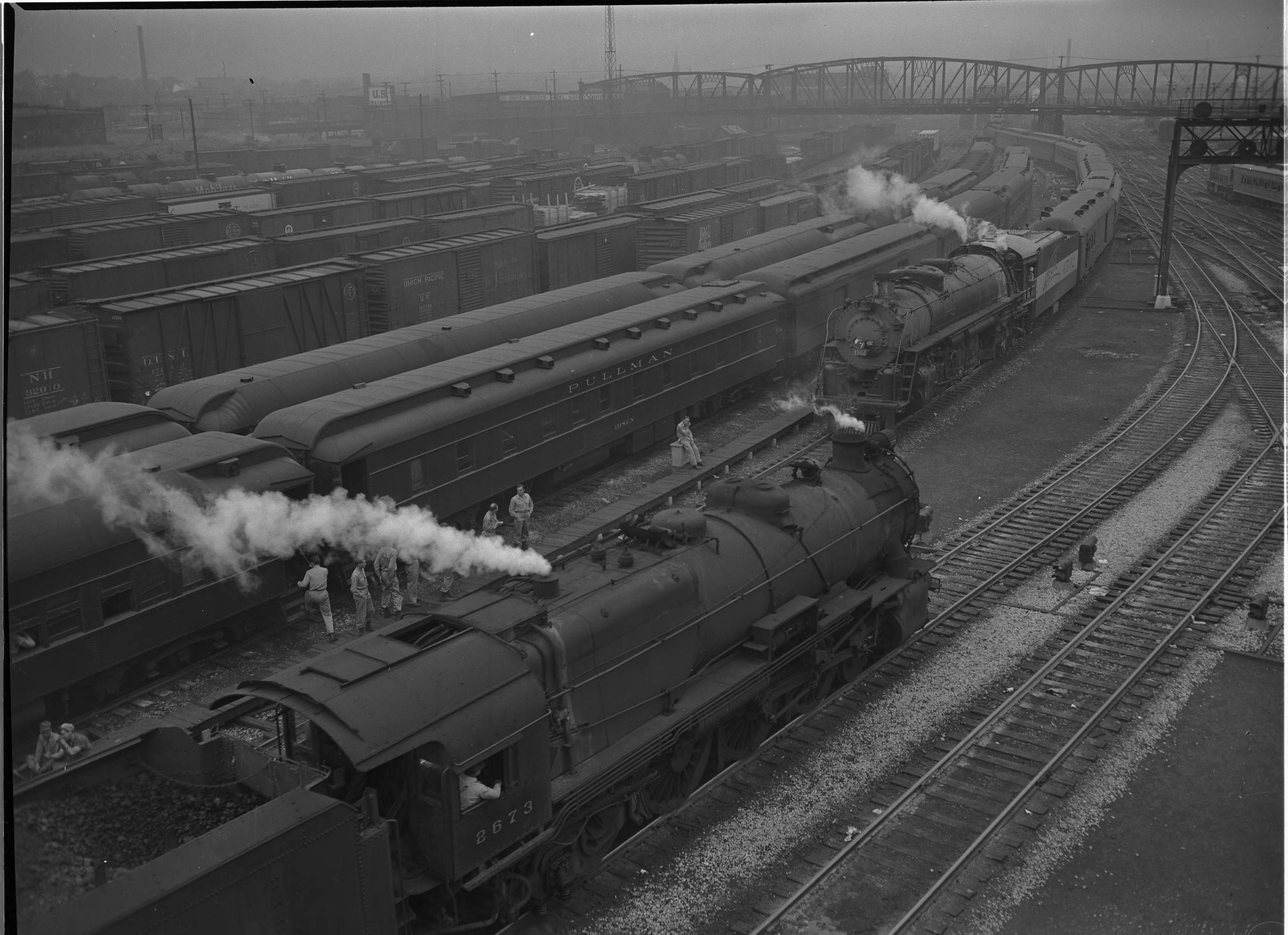 Two steam trains pass each other in a busy St. Louis railyard