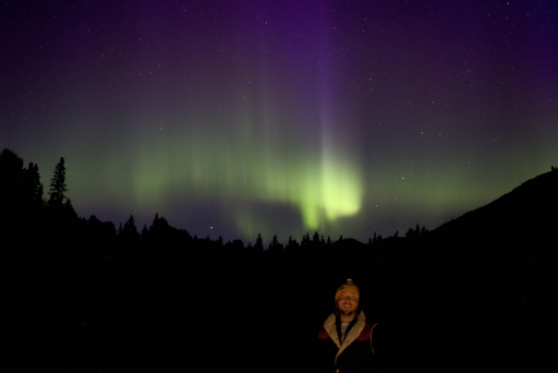 Bright yellow flares under the purple beams of the northern lights.  Selfie taken using a small camp light between me and the camera.  